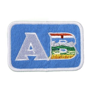 May include: A blue embroidered patch with the letters "AB" in white. The "B" is styled to include the flag of Alberta, Canada.