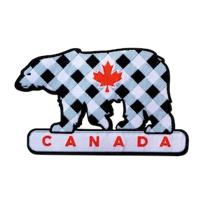 May include: A white and black checked bear with a red maple leaf on its chest. The bear is standing on a white banner with the word "CANADA" in black letters.