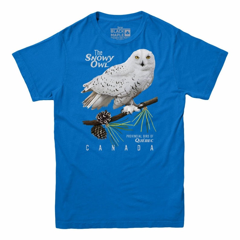 May include: A blue t-shirt with a white snowy owl perched on a branch with pine cones. The text "The Snowy Owl" is above the owl and "Provincial Bird of Quebec CANADA" is below the owl.