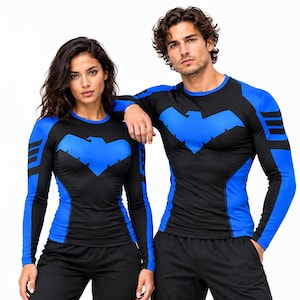 May include: A long-sleeve compression shirt featuring a black base with vibrant blue panels on the sleeves and sides. A stylized blue bird emblem is centered on the chest. The sleeves include three horizontal blue stripes near the shoulders.