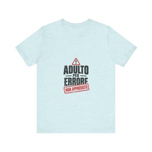 Può includere: Una t-shirt a maniche corte color azzurro con un design grafico che presenta un triangolo di avvertimento rosso con un punto esclamativo, il testo ADULTO PER ERRORE in nero e un timbro rettangolare rosso con il testo NON APPROVATO.