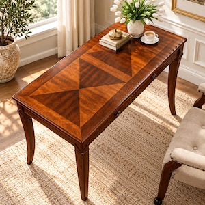 May include: A rectangular wooden writing desk with a rich brown finish and a geometric triangular veneer pattern on the tabletop. The desk features four tapered legs and a single drawer with a small, dark metal knob handle.