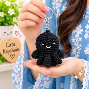 May include: A black crocheted octopus keychain featuring a round head, eight small tentacles, and two glossy black eyes with a white stitched mouth. The plush octopus is attached to a silver metal split ring by a short silver chain.