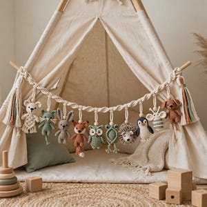 May include: A macrame garland featuring a series of small, crocheted animal figures including a bear, cat, rabbit, fox, owl, frog, hedgehog, penguin, bee, and dog, suspended from a twisted cotton cord with decorative tassels at each end.