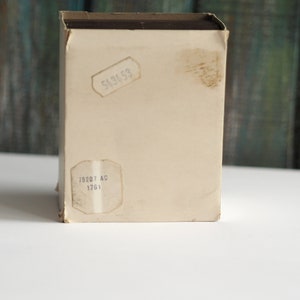 May include: A white cardboard box with brown tape and two labels. The top label says "543653" and the bottom label says "75207 AC 1761".