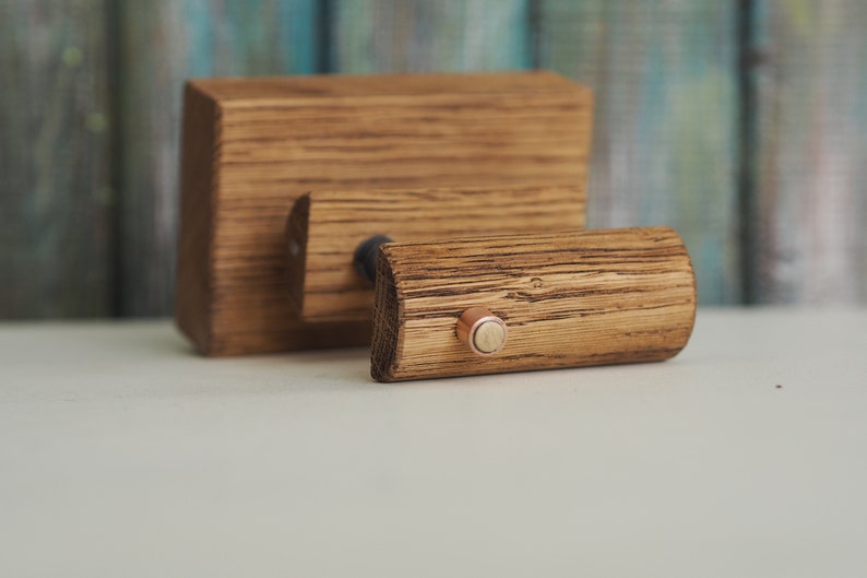May include: A wooden wall mount with a single hook. The hook is made of a dark wood and has a copper accent. The wall mount is made of a lighter wood and has a natural finish.