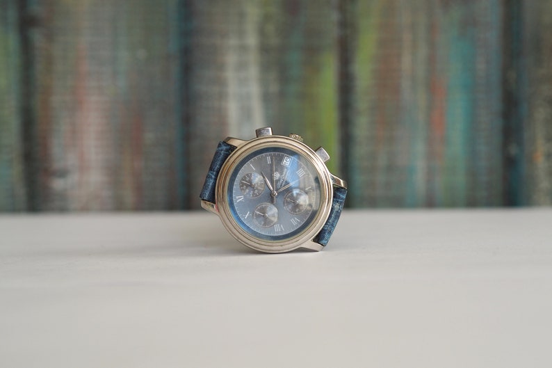 Pu&ograve; includere: Un orologio da polso cronografo argentato con quadrante blu e cinturino in denim blu.
