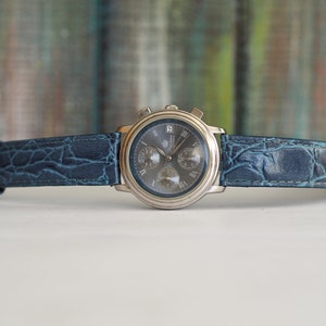 Pu&ograve; includere: Un orologio da polso cronografo argentato con quadrante blu e cinturino in pelle blu con stampa coccodrillo.