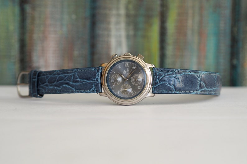Pu&ograve; includere: Un orologio da polso cronografo argentato con quadrante blu e cinturino in pelle blu con stampa coccodrillo.