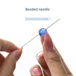 May include: A long, thin metal beading needle with a single translucent blue spherical bead threaded onto the center. The text Beaded needle and Convenient and practical/easy beading are visible above the needle and bead.