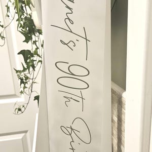 以下が含まれることがあります： 「Janet's 90th Birthday」と黒文字で書かれた白いバナー