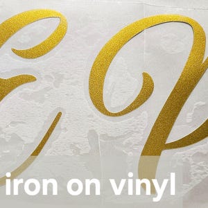 May include: Gold iron-on vinyl letters spelling "EP" on a white background. The letters are in a cursive font.