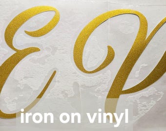 May include: Gold iron-on vinyl letters spelling "EP" on a white background. The letters are in a cursive font.