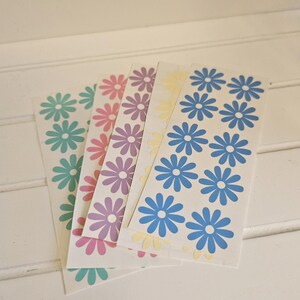 May include: Four sheets of stickers with daisy designs in blue, yellow, purple, and pink.