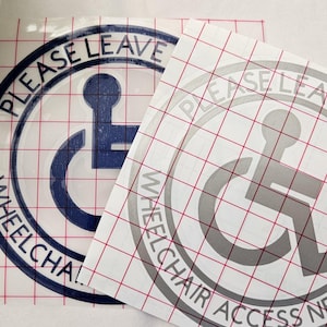 May include: Two vinyl stickers with a wheelchair symbol and the text "Please Leave Room Wheelchair Access Needed". The stickers are on a gridded transfer sheet.