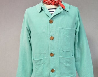 May include: A light green work jacket with four brown buttons and two large pockets. The jacket is on a white mannequin with a red bandana and a striped shirt underneath.