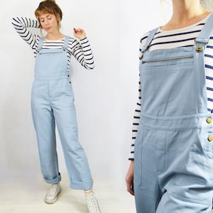 May include: A light blue denim overall with a zipper detail and button closures. The overall has a relaxed fit and wide legs.