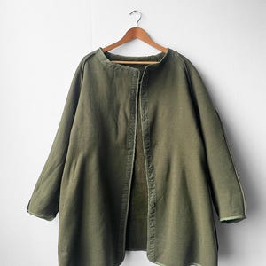 Puede incluir: Una chaqueta verde de manga larga con botones y cuello. La chaqueta tiene un corte holgado y está hecha de un tejido suave y texturizado.