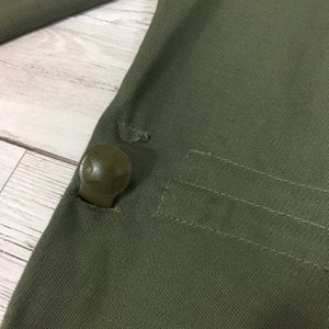 May include: Close-up of a green canvas fabric with a plastic button. The button has a star-shaped design.