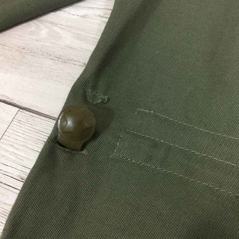 May include: Close-up of a green canvas fabric with a plastic button. The button has a star-shaped design.