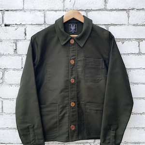 Puede incluir: Una chaqueta de manga larga color verde oliva con cuello clásico, cierre frontal de botones en color marrón claro, dos bolsillos de parche inferiores y un bolsillo en el pecho. La etiqueta interior muestra un gráfico de lobo y el texto WOLF.