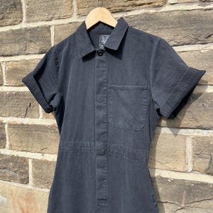 K&ouml;nnte beinhalten: Ein schwarzer Kurzarm-Overall mit Knopfleiste und einer Brusttasche.