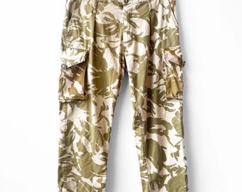 May include: Camouflage cargo pants with a brown and beige pattern. The pants have two large pockets on the sides.