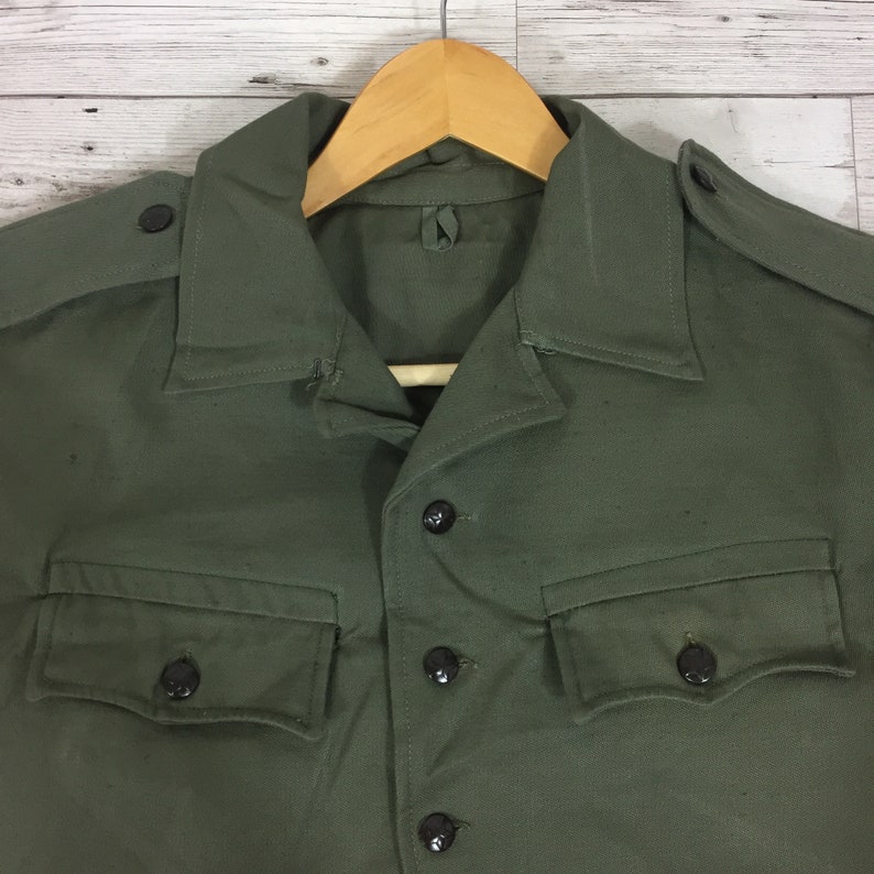 May include: A green military-style shirt with a button-up front and two flap pockets. The shirt has a collar and is made of a durable fabric.