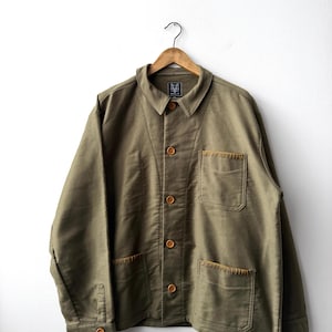 以下が含まれることがあります： オリーブグリーンのボタンアップジャケット。尖った襟、ボタン付きカフスの長袖、3つのパッチポケットが特徴です。ポケットの上端にはベージュの装飾ステッチが施されています。首元には小さなラベルが付いています。