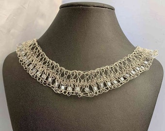 May include: A silver wire necklace with small, clear beads. The necklace is on a black mannequin bust.