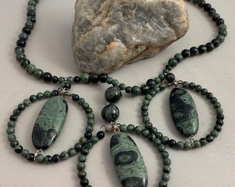 May include: A green and black stone necklace with three oval-shaped pendants. The necklace is made of small, round beads and has a simple design.