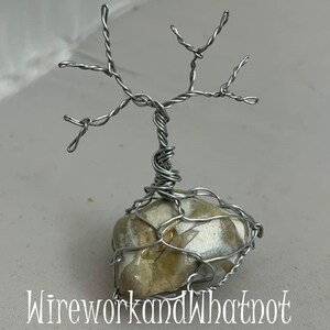 May include: A silver wire tree sculpture with a brown and white stone base. The tree has many branches and is wrapped in wire. The stone is encased in wire.