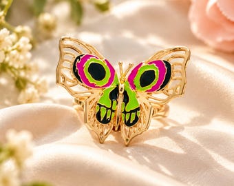 Kleurrijke vlinderring met goudkleurige emaille vlinder, statement sieraad met levendige roze en groene vleugels, speels natuuraccessoire, uniek cadeau voor vlinderliefhebbers.