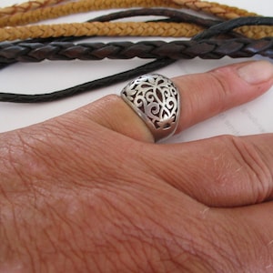 以下が含まれることがあります： 透かし模様の入った銀の指輪。指輪は指にはめられています。