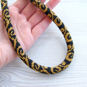 May include: A black and gold beaded necklace with a geometric pattern. The necklace is made of small beads and is about 18 inches long.