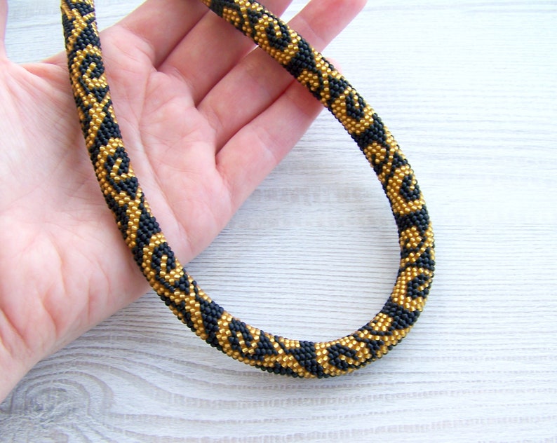 May include: A black and gold beaded necklace with a geometric pattern. The necklace is made of small beads and is about 18 inches long.