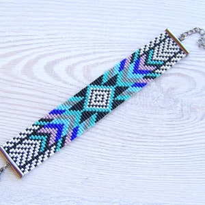 Puede incluir: Un brazalete de cuentas con un patr&oacute;n geom&eacute;trico en tonos de azul, blanco, negro y gris. El brazalete tiene un cierre plateado.