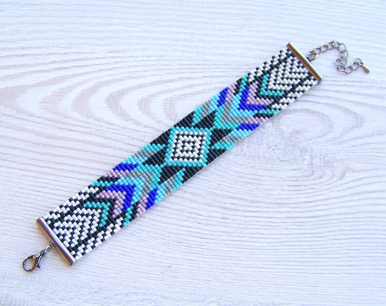 Puede incluir: Un brazalete de cuentas con un patr&oacute;n geom&eacute;trico en tonos de azul, blanco, negro y gris. El brazalete tiene un cierre plateado.