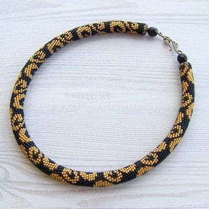 May include: A black and gold beaded necklace with a geometric pattern. The necklace has a clasp closure.