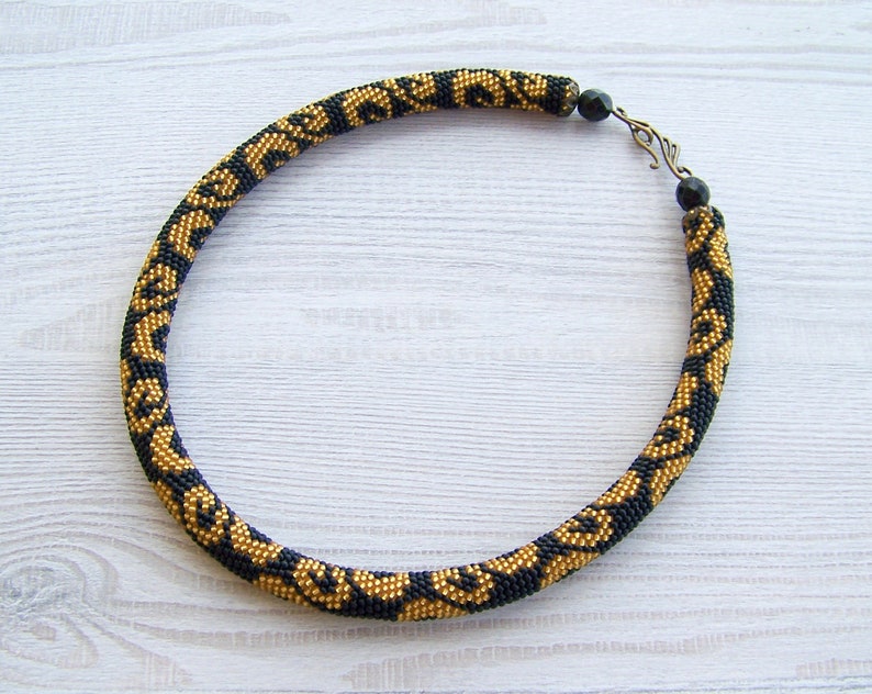 May include: A black and gold beaded necklace with a geometric pattern. The necklace has a clasp closure.