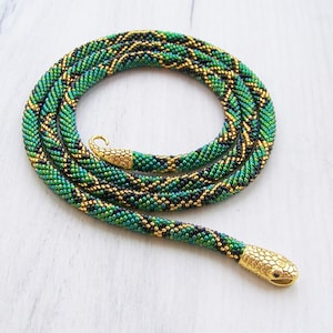 Könnte beinhalten: Eine grüne und goldene Perlenkette in Schlangenform mit einem goldenen Schlangenkopf-Anhänger.