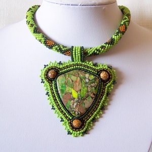 May include: A green, brown, and black beaded necklace with a triangular pendant featuring a green and brown stone.