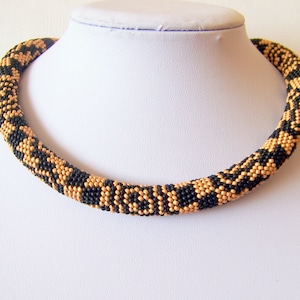 May include: A black and gold beaded necklace with a geometric pattern. The necklace is made of small, round beads that are woven together to create a unique design.