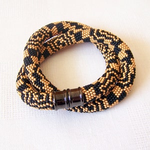 May include: A black and gold beaded necklace with a magnetic clasp. The beads are arranged in a geometric pattern.