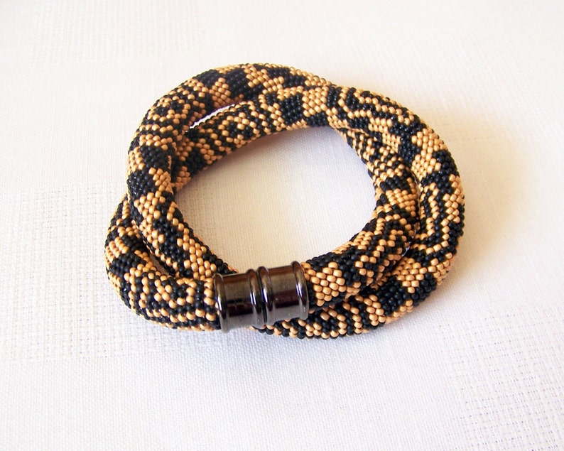 May include: A black and gold beaded necklace with a magnetic clasp. The beads are arranged in a geometric pattern.