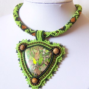 May include: A green and brown beaded necklace with a triangular pendant featuring a green and brown stone.