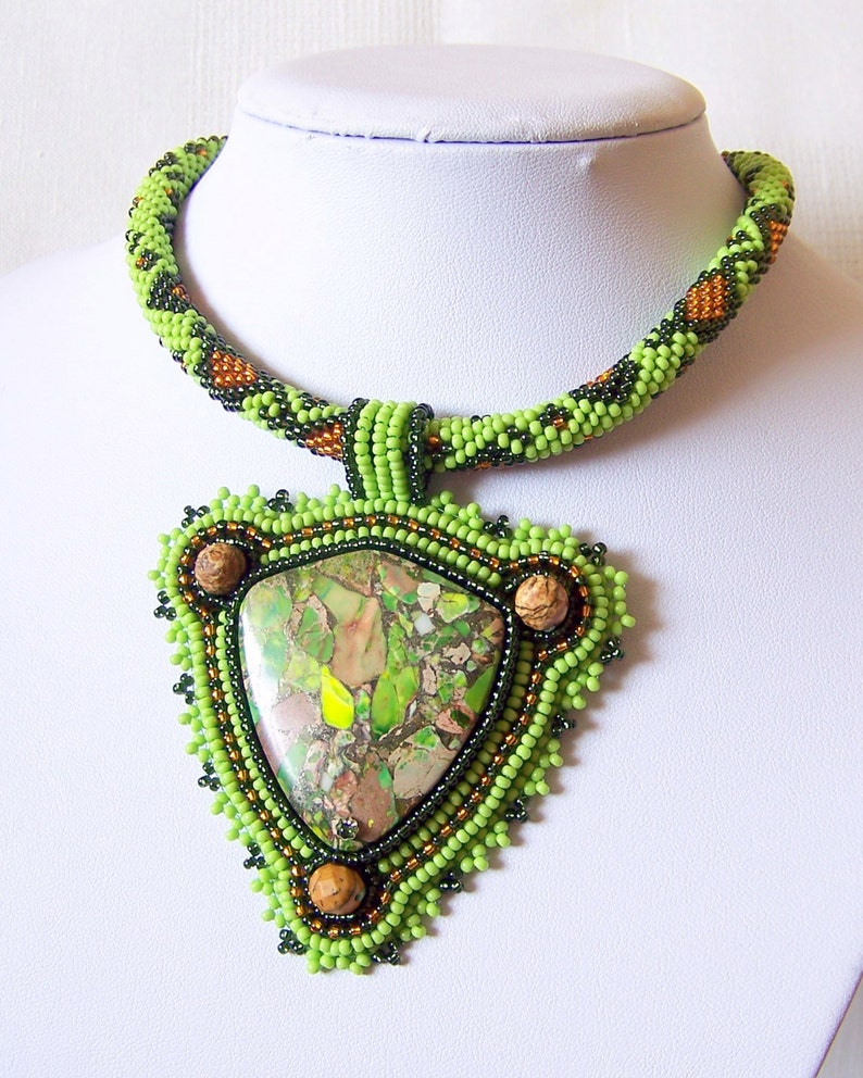 May include: A green and brown beaded necklace with a triangular pendant featuring a green and brown stone.