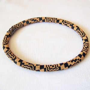 May include: A black and gold beaded necklace with a magnetic clasp. The necklace is made of small, round beads that are arranged in a geometric pattern.
