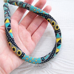 May include: A beaded necklace with a geometric pattern in black, gray, yellow, and turquoise.