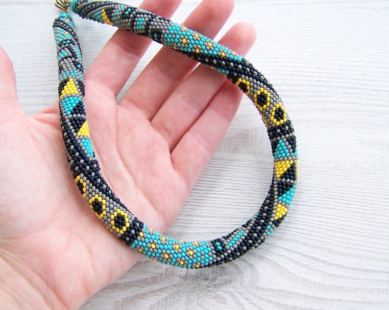 May include: A beaded necklace with a geometric pattern in black, gray, yellow, and turquoise.